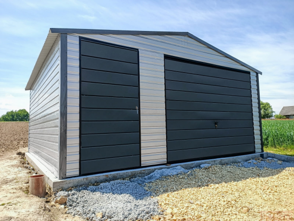 Metal garage with a gable roof featuring silver side panels and contrasting dark gray front doors on a gravel and concrete base.