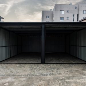 Dual-bay matte black metal garage with open doors in an urban residential setting.