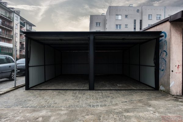 Dual-bay matte black metal garage with open doors in an urban residential setting.