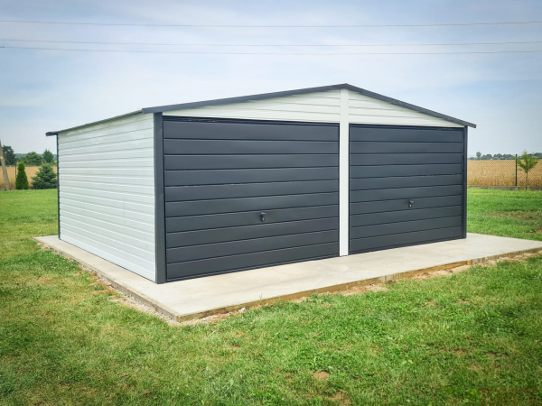 Two-door metal garage with white side panels and matte black front doors, placed on a concrete slab in a grassy field.