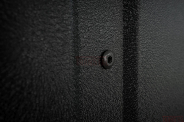 Close-up of a matte black rivet on textured metal siding.