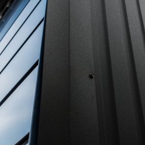 Close-up of matte black metal siding with textured finish and a visible wall screw.