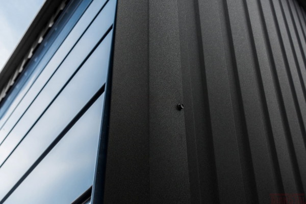 Close-up of matte black metal siding with textured finish and a visible wall screw.