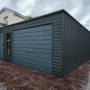 Modern matte black metal garage with flat roof, horizontal panel door, side access door, and vertical window, placed next to a cream house on a tiled driveway.