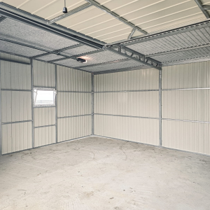 Interior of a spacious metal garage with light-colored corrugated walls, window, and reinforced roof framing.