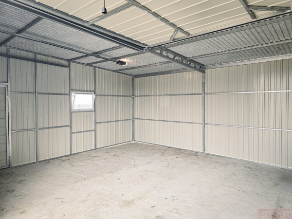Interior of a spacious metal garage with light-colored corrugated walls, window, and reinforced roof framing.